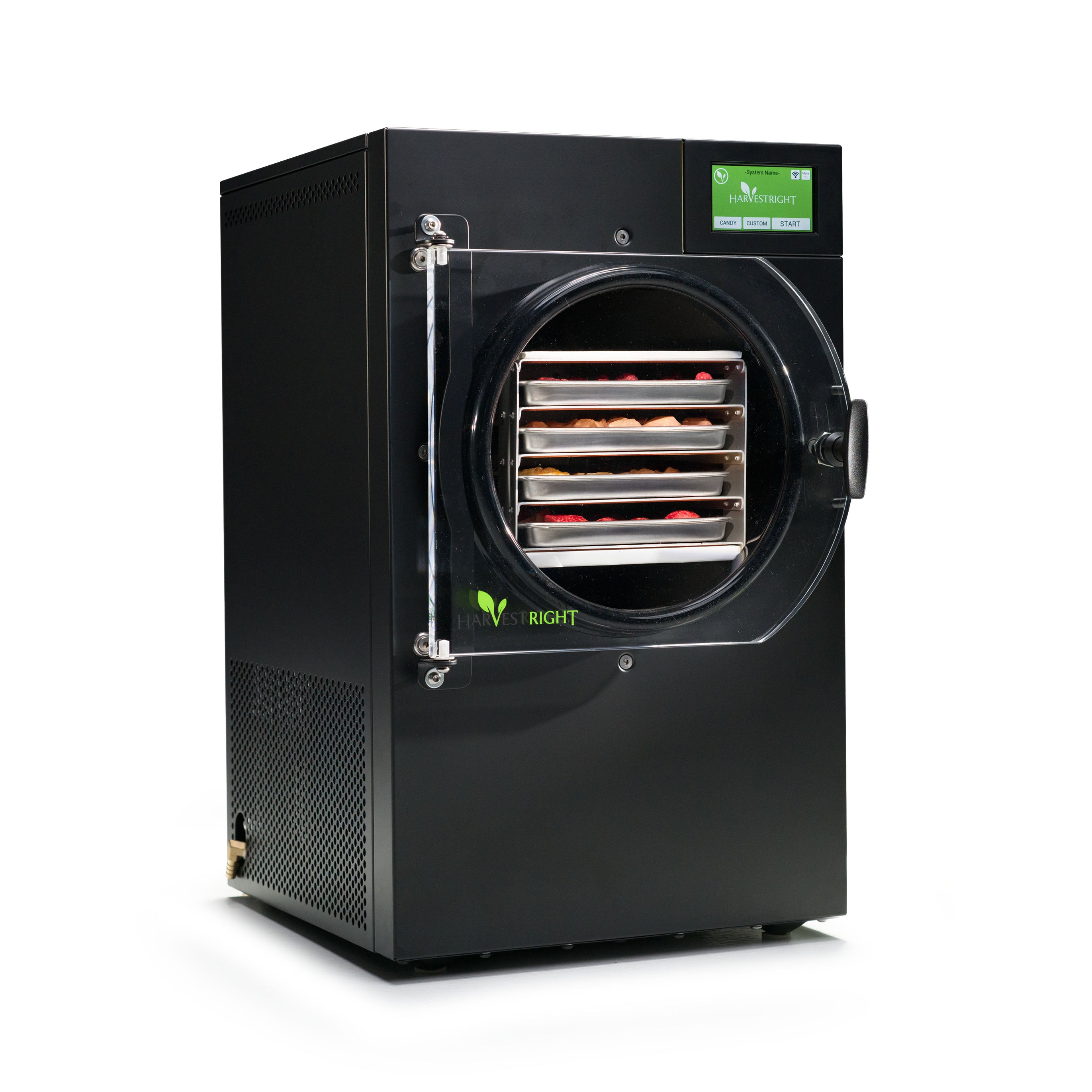 A black Harvest Right home freeze dryer with its clear door closed, four stainless steel trays of raspberries and other food visible inside the vacuum chamber, and a green touchscreen showing Candy, Custom and Start